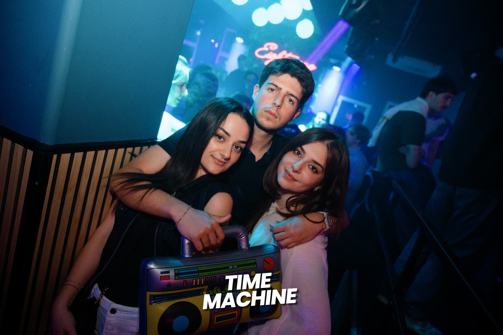 Three friends posing with a boombox prop at a Time Machine night