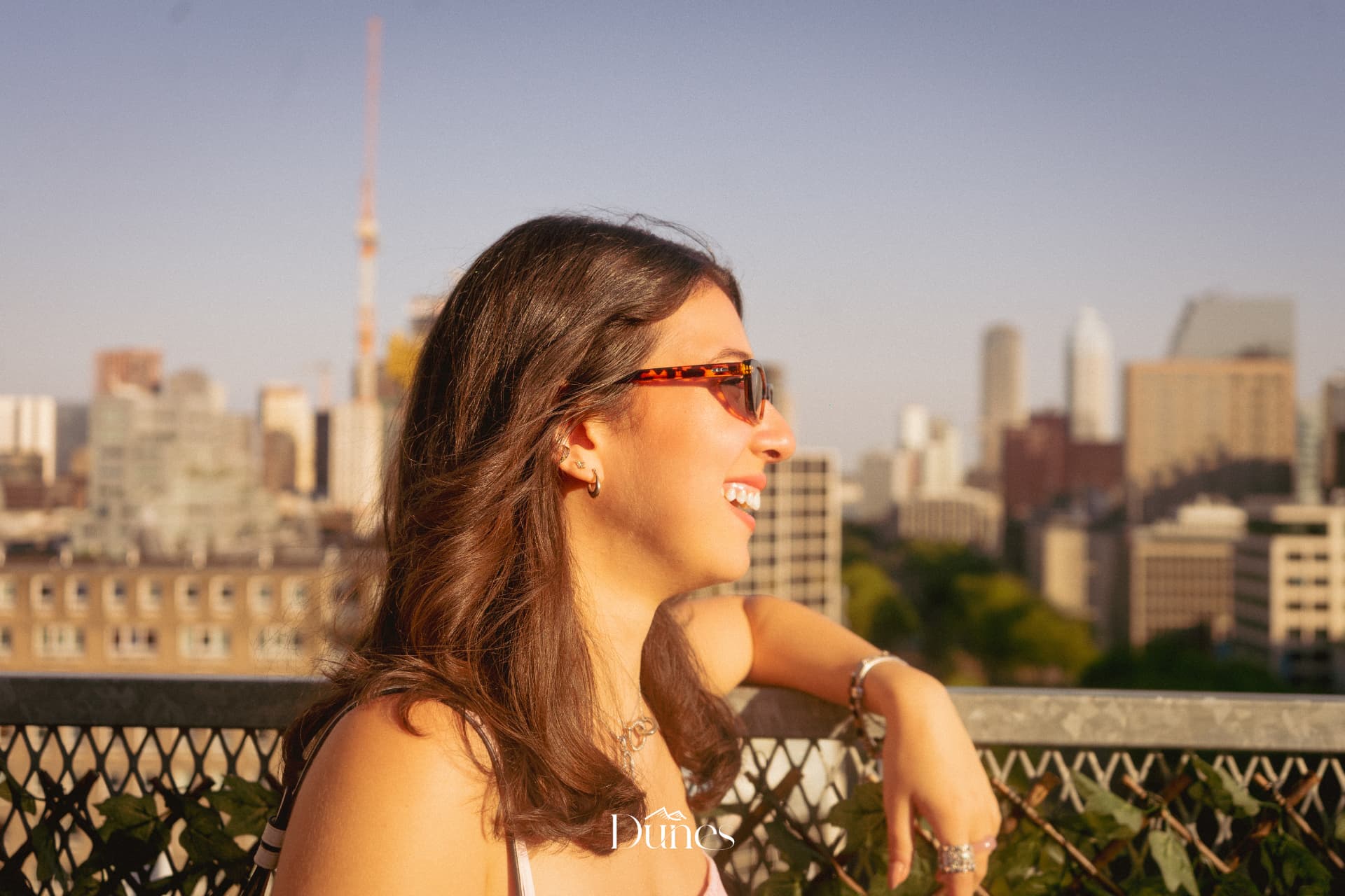 Guest smiling on a rooftop at golden hour with the city skyline behind her